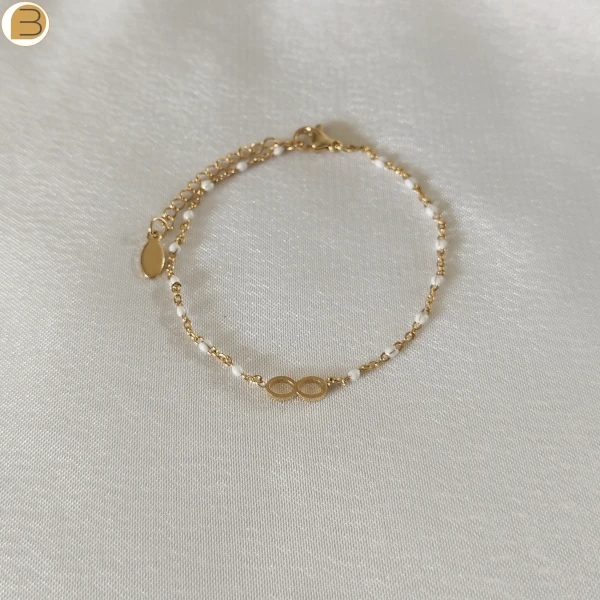 Bracelet en acier inoxydable doré pour femme avec ses fines perles blanches et son pendentif infini.