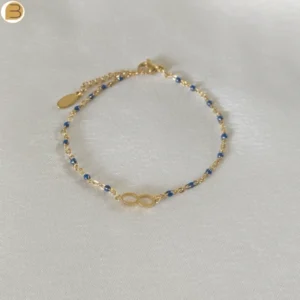 Bracelet en acier inoxydable doré pour femme avec ses fines perles bleues et son pendentif infini.