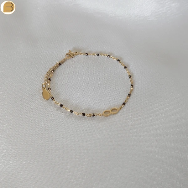 Bracelet en acier inoxydable doré pour femme avec ses fines perles noires et son pendentif infini.
