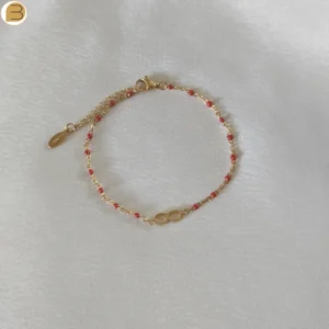 Bracelet en acier inoxydable doré pour femme avec ses fines perles rouges et son pendentif infini.
